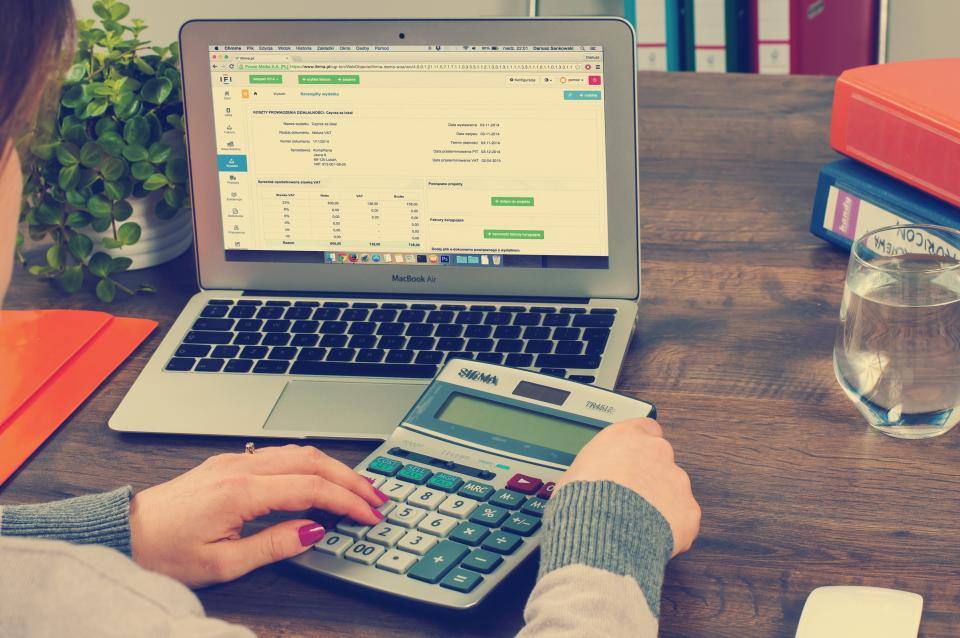 Duar që punojnë me makinë llogaritëse pranë një laptopi me tabelë financiare